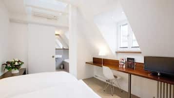 Ein modernes Hotelzimmer mit einem großen Bett, einem Schreibtisch mit Stuhl, einem Fernseher und einem Dachfenster.