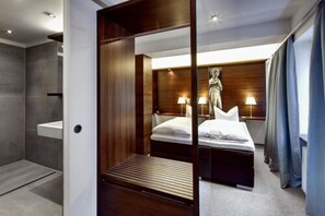 A modern hotel room with a bed, bedside lamps, a wooden headboard, and a shower area. - Stern am Rathaus (Cologne)