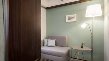 Ein Zimmer mit einer Couch, einem kleinen Tisch mit Lampe und einem Bild an der Wand.