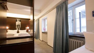 Una habitación de hotel con una cama, un espejo, una estatua, una ventana con cortinas y un radiador.