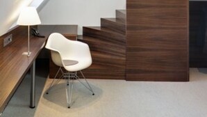 A modern interior with a sloped ceiling, a wooden accent wall, a white chair, and a desk with a lamp. - Stern am Rathaus (Cologne)