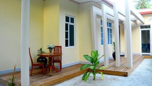 Una zona patio coperta con tavolo e sedie in legno, piante in vaso e vista sull'edificio limitrofo.