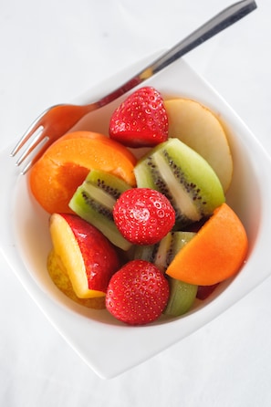 A bowl of fruit including strawberries, kiwi, and melon slices.