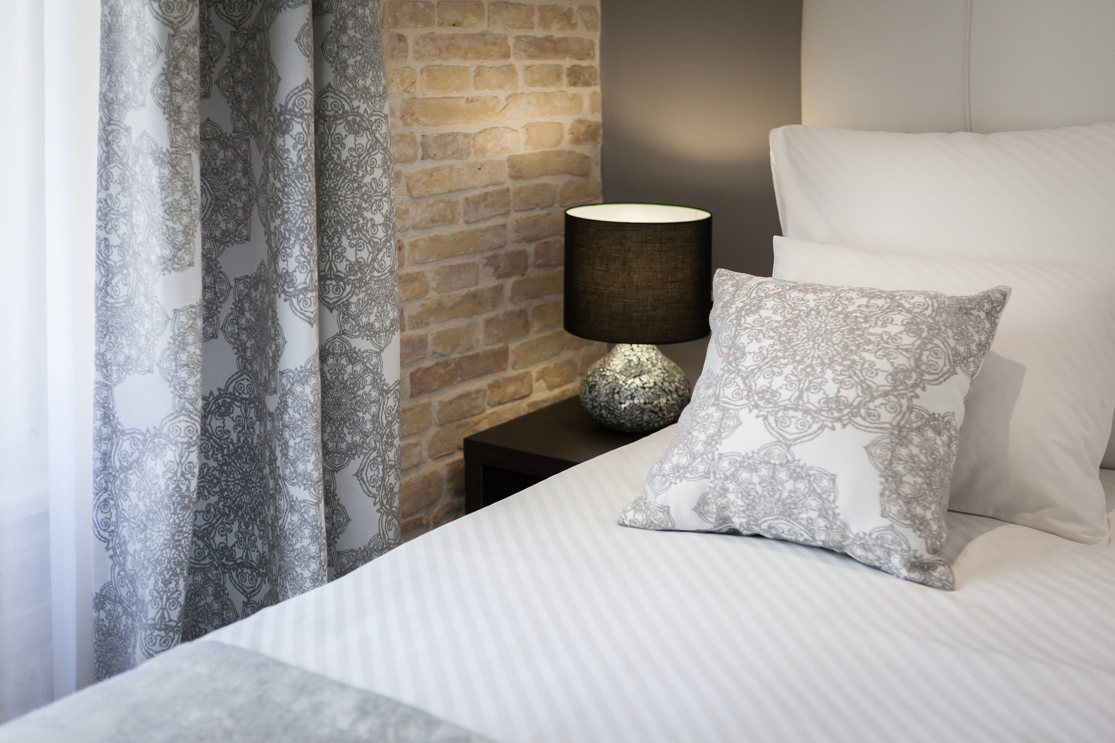 A neatly made bed with a patterned pillow and a lamp on a nightstand.