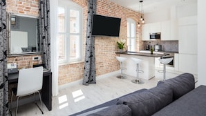 Une cuisine moderne avec un mur en briques, des meubles blancs, un téléviseur à écran plat et un coin bar avec des tabourets.