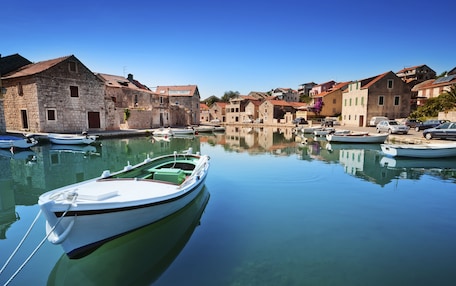 A calm harbor with boats docked, stone buildings, and clear blue skies.