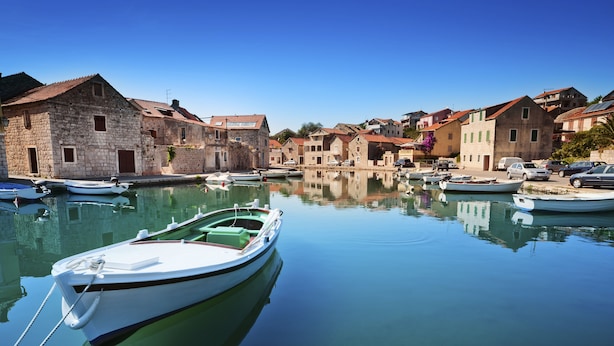 Un port tranquille, avec des bateaux amarrés, des bâtiments en pierre et un ciel bleu dégagé.