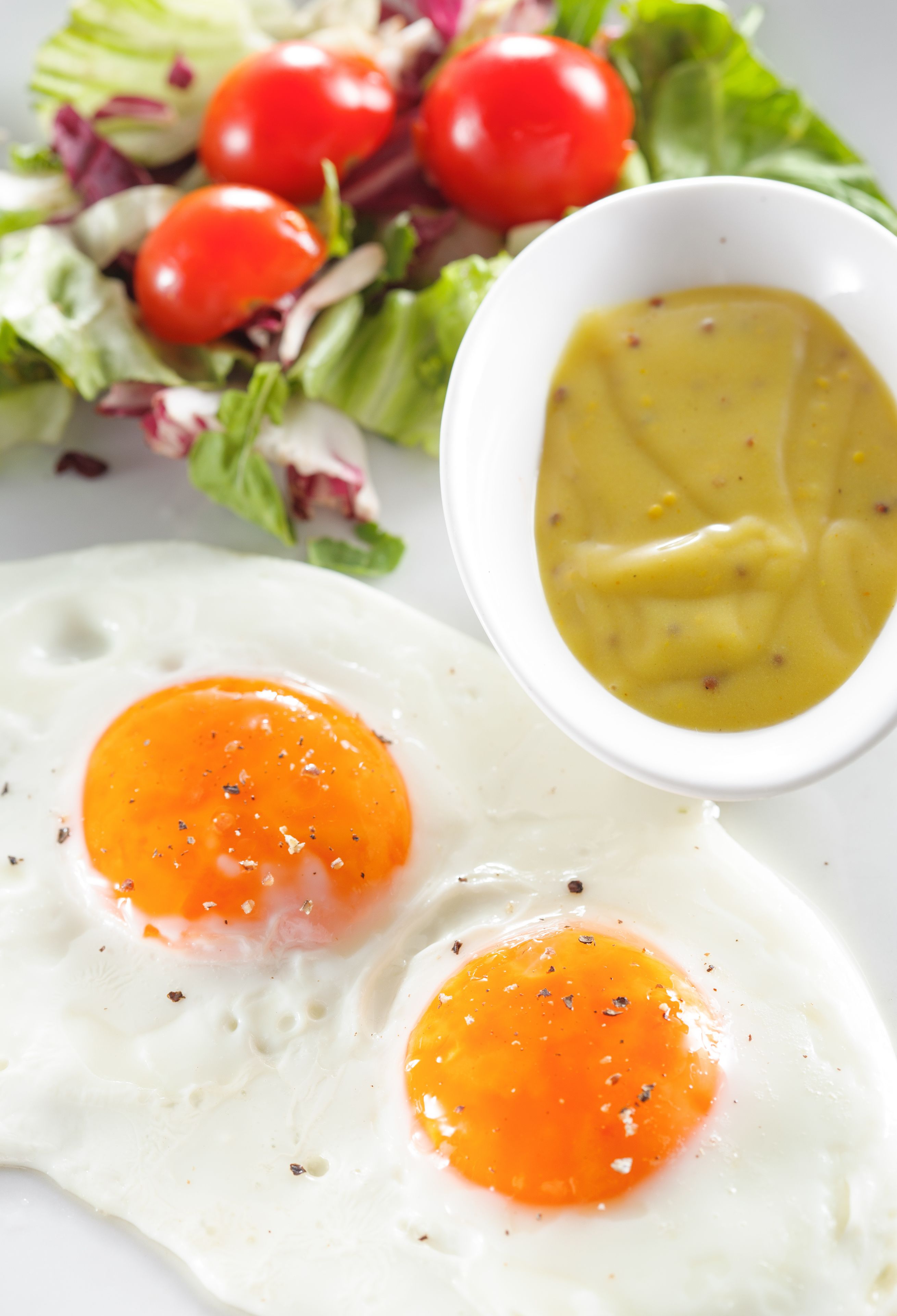 A plate with two sunny-side-up eggs, a side salad, and a bowl of mustard sauce.