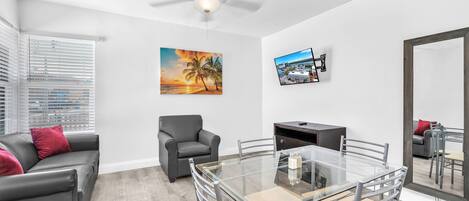 A modern living room with a glass dining table, grey sofa, and a ceiling fan.
