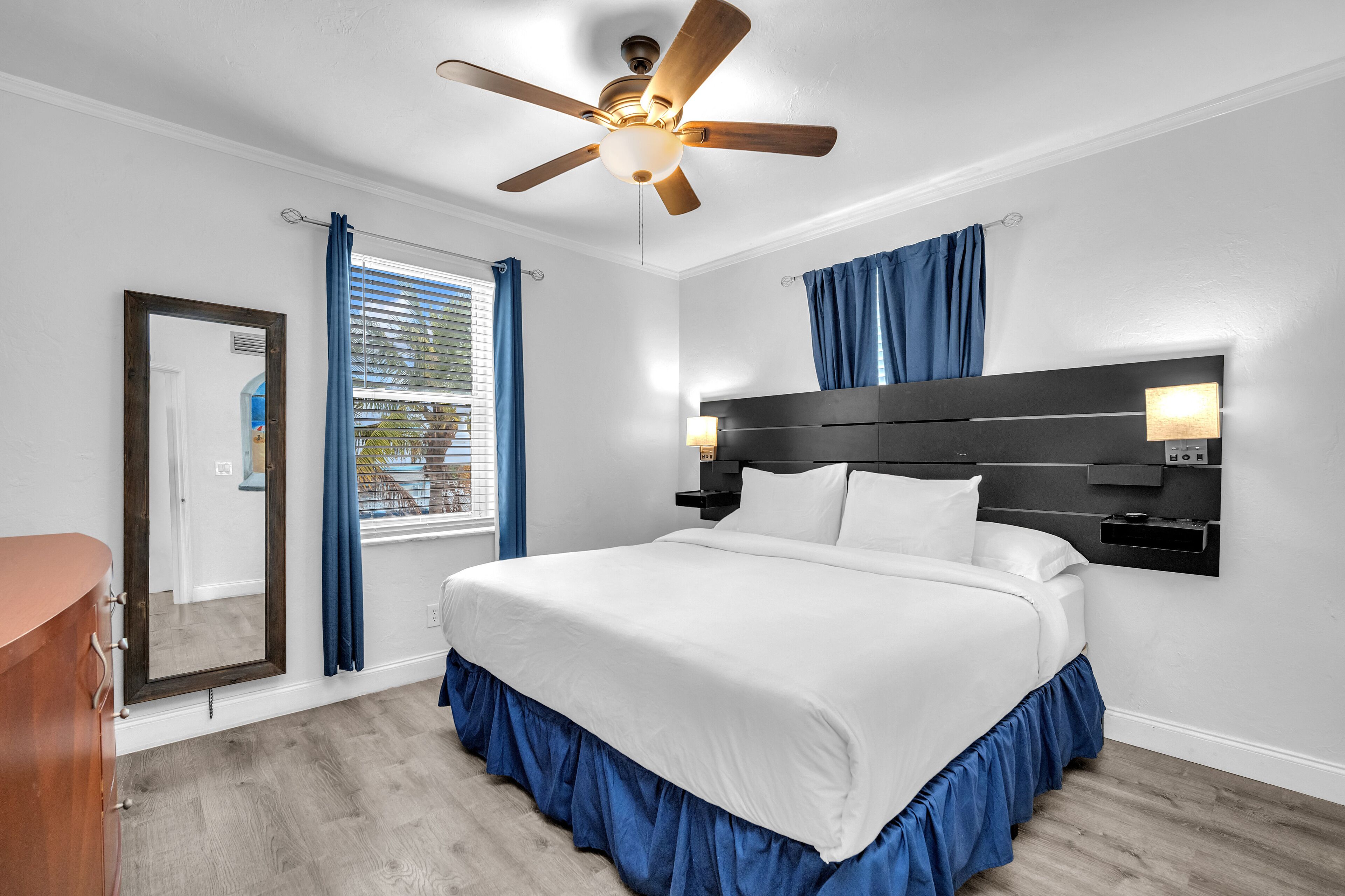 Una camera da letto con un letto grande, una ventola a soffitto, un comodino con una lampada e una finestra con tende.