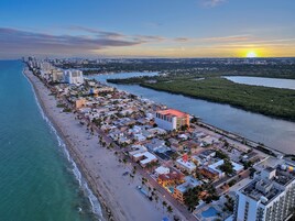 A coastal cityscape with a beachfront hotel, a marina, and a sunset over the ocean.