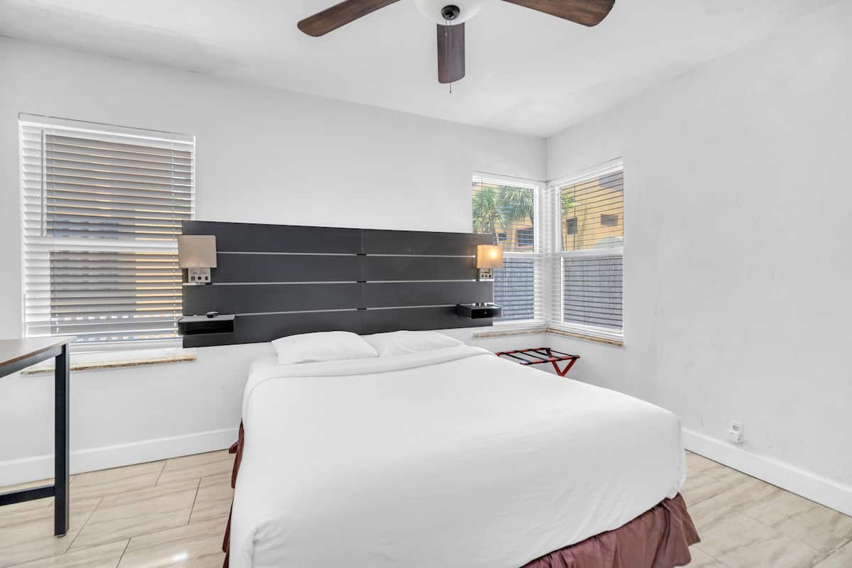 Un dormitorio moderno con una cama grande, un ventilador de techo y dos ventanas con persianas.