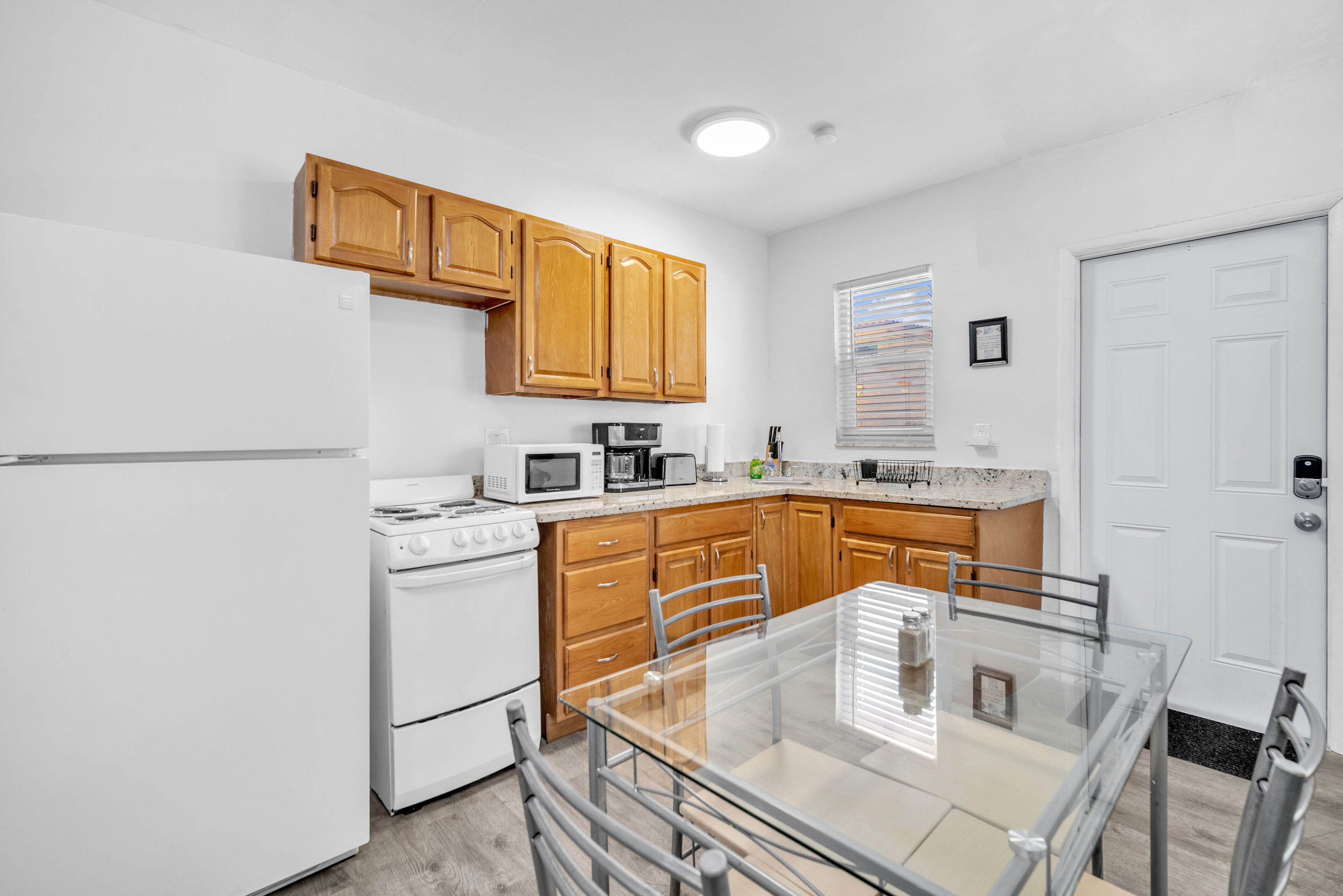 A modern kitchen with white appliances, wooden cabinets, and a glass dining table.