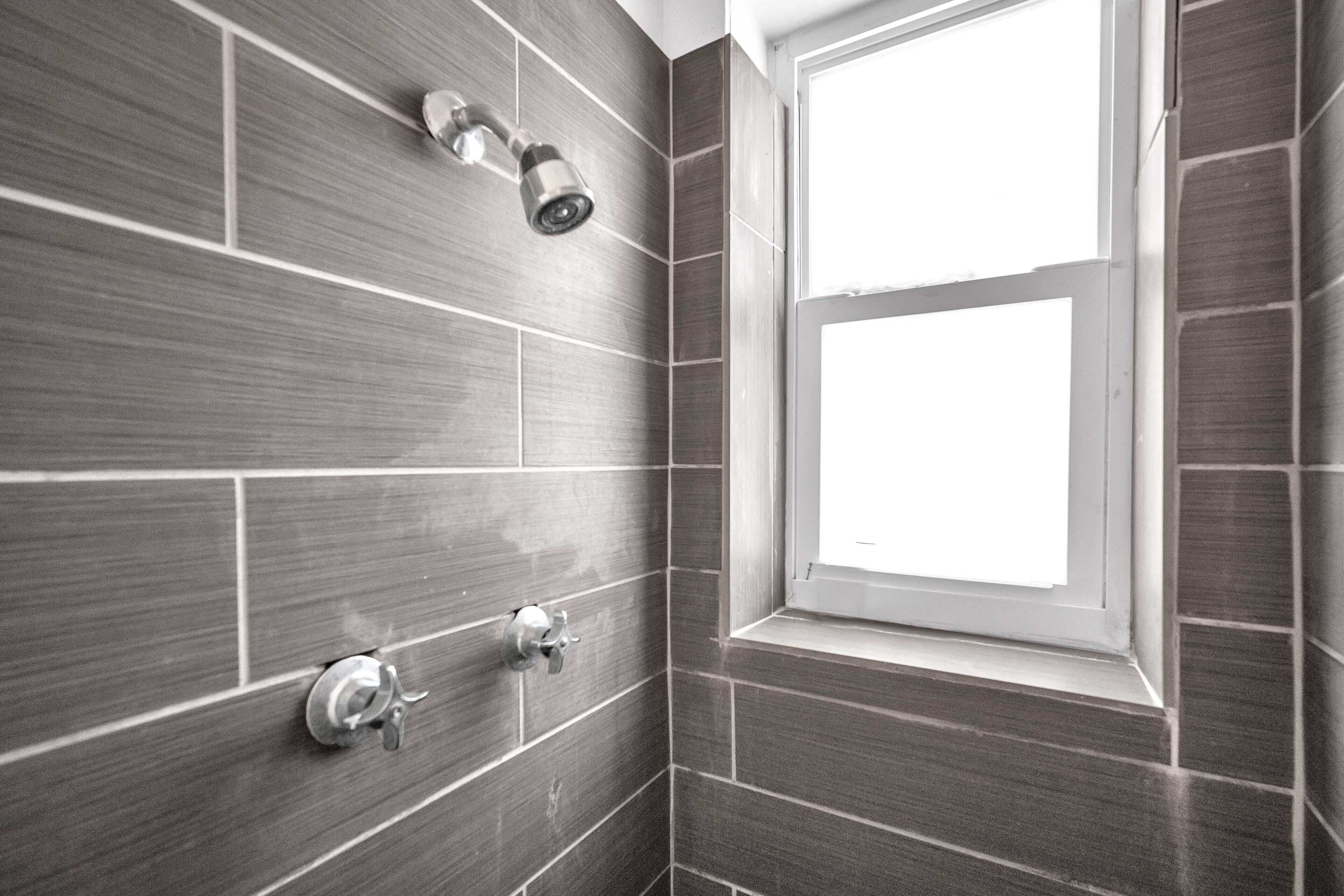 A bathroom with dark tiles, a window, and a showerhead.