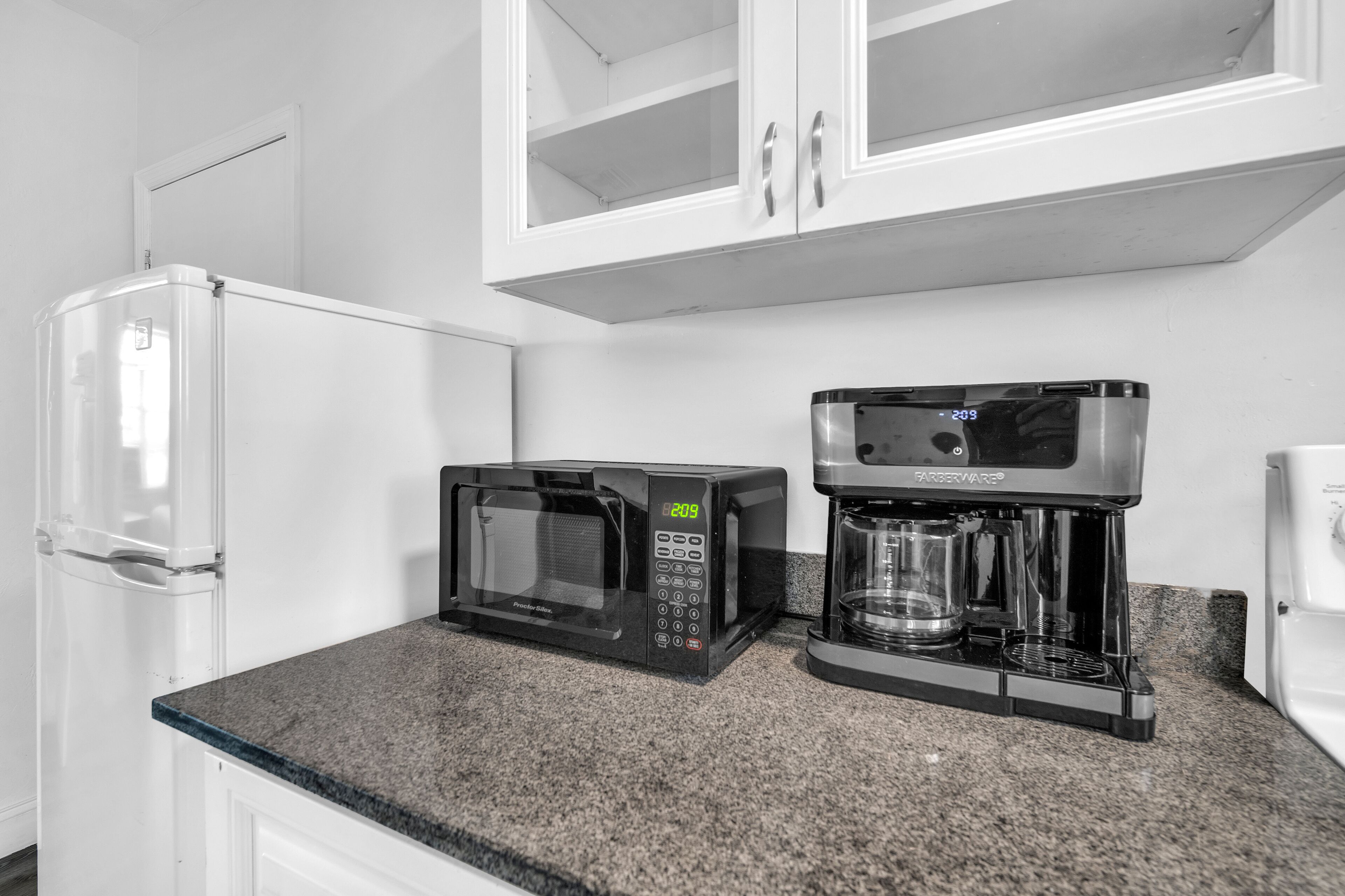 A kitchen with a refrigerator, a microwave, and a coffee maker on a granite countertop.