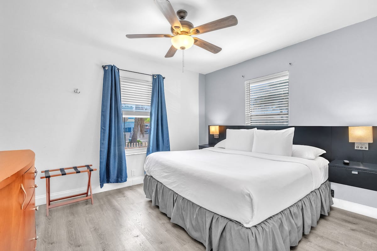 Un dormitorio moderno con una cama grande, un ventilador de techo y vistas al exterior a través de una ventana.