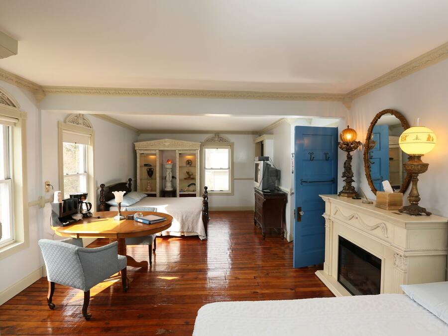 Una habitación con piso de madera, una cama, un escritorio con una silla, una chimenea y una puerta azul.