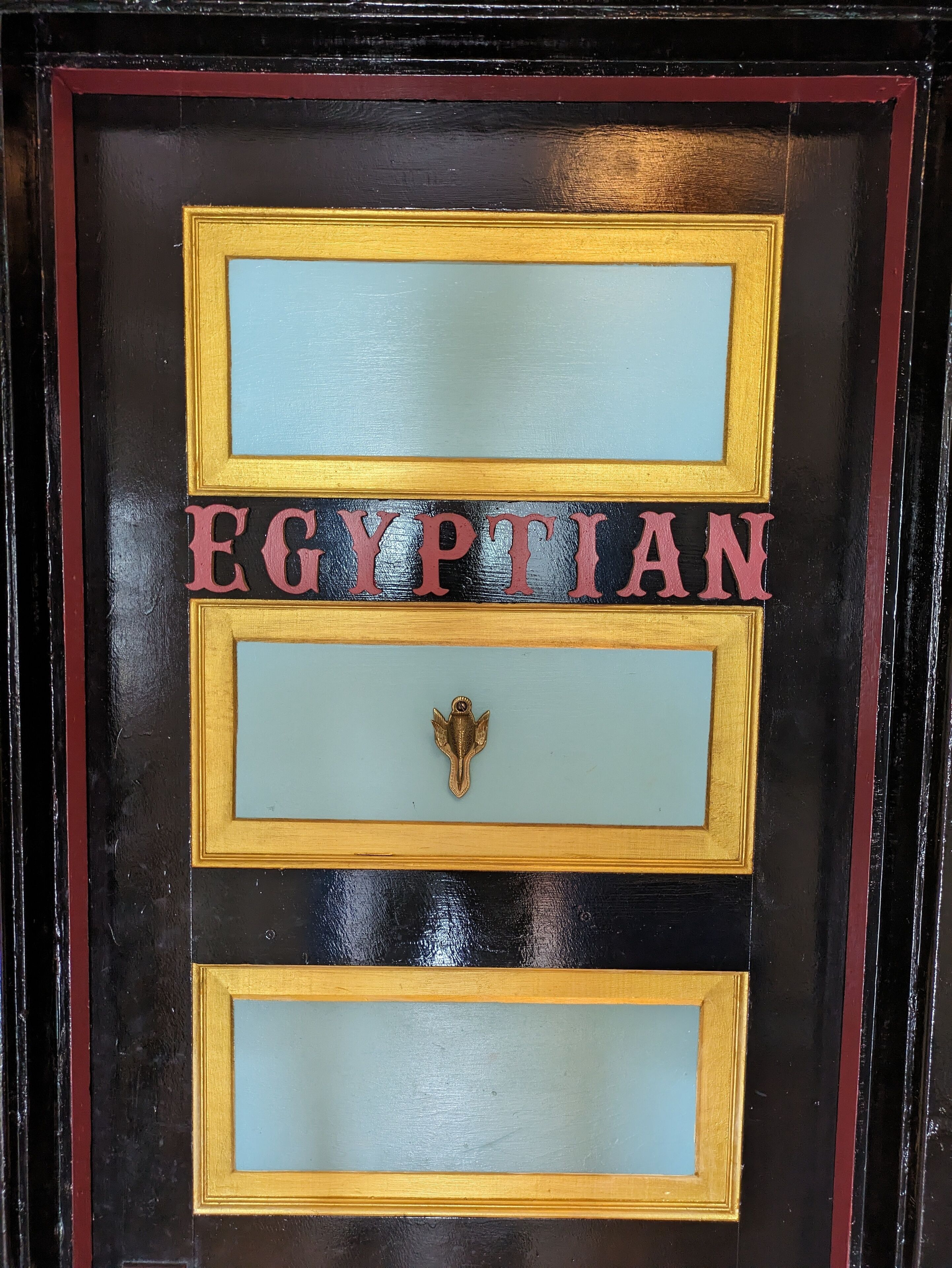 A door with the word "EGYPTIAN" in large letters, a brass handle, and a decorative frame.