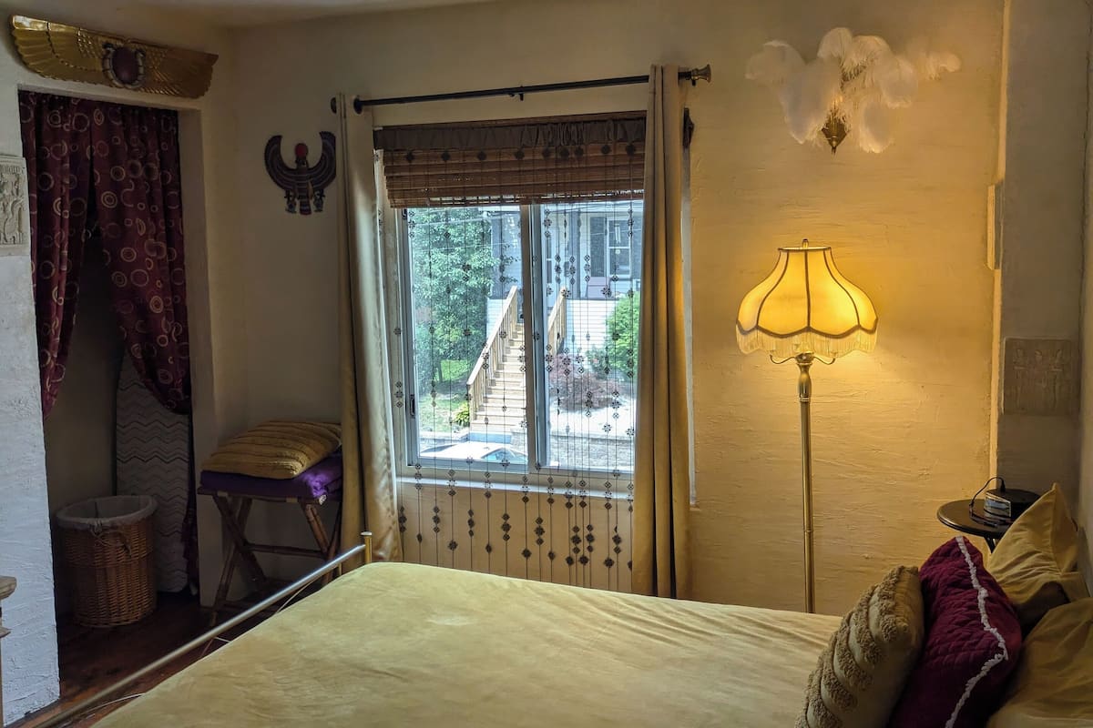 A bedroom with a bed, a window with curtains, a lamp, and a wall decoration.