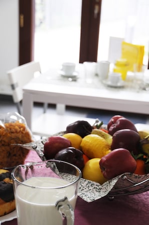 A dining table with a glass pitcher of milk, a basket of assorted fruits, and a bag of cereal. - La Circumetnea B&B (Catania)