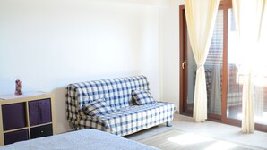 A bedroom with a bed, a checkered sofa, a small table with a vase, and a sliding glass door leading to a balcony. - La Circumetnea B&B (Catania)