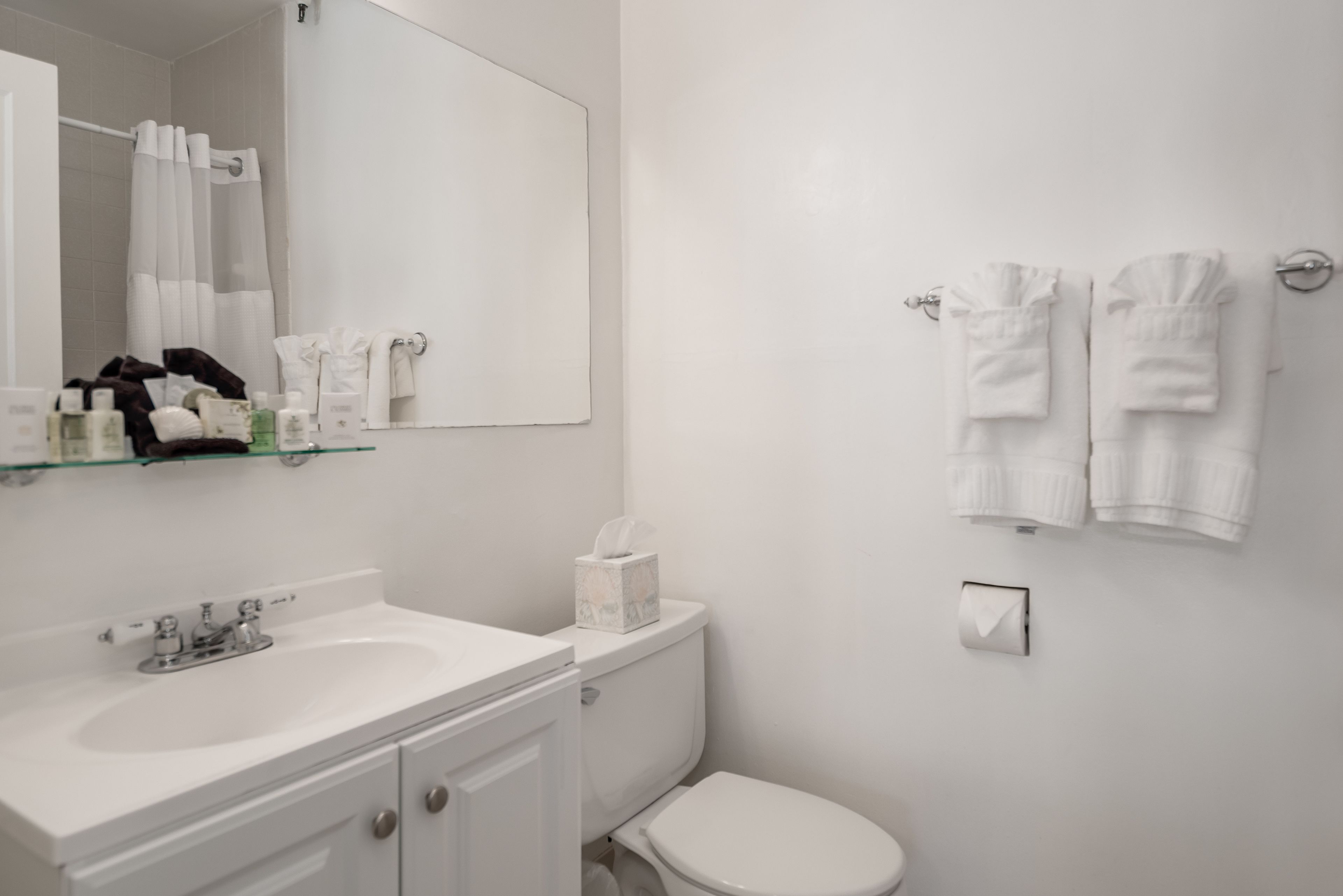 A bathroom with a white sink, mirror, and toilet. There are towels and toiletries on the counter.