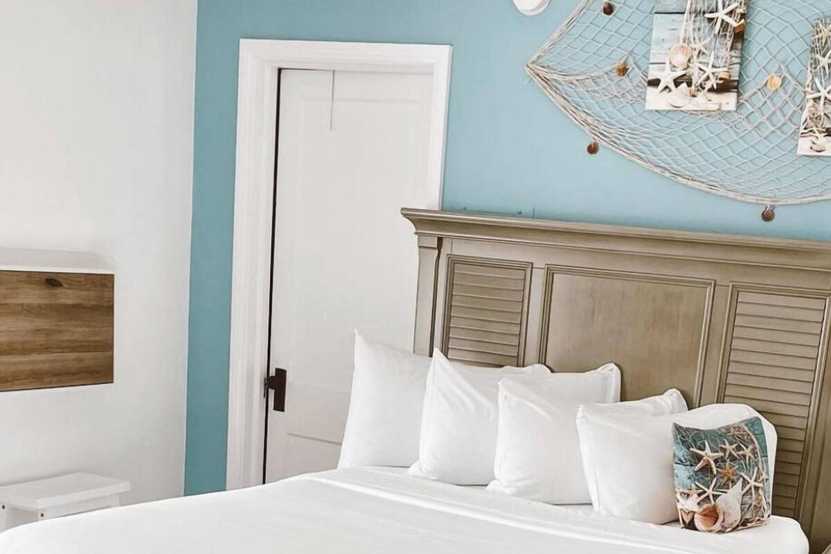 A bedroom with a large bed, a wooden headboard, a white door, and a wall-mounted decoration.