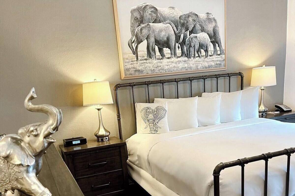 A bedroom with a bed, two bedside tables, a lamp, a framed picture on the wall, and a decorative elephant figurine.