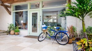 A blue bicycle with a basket and a wicker bag parked outside a building with a green door and windows. - Palm Beach Historic Inn (Palm Beach)