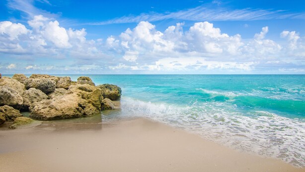 A beach with clear turquoise water, white sand, and large rocks. - Palm Beach Historic Inn (Palm Beach)