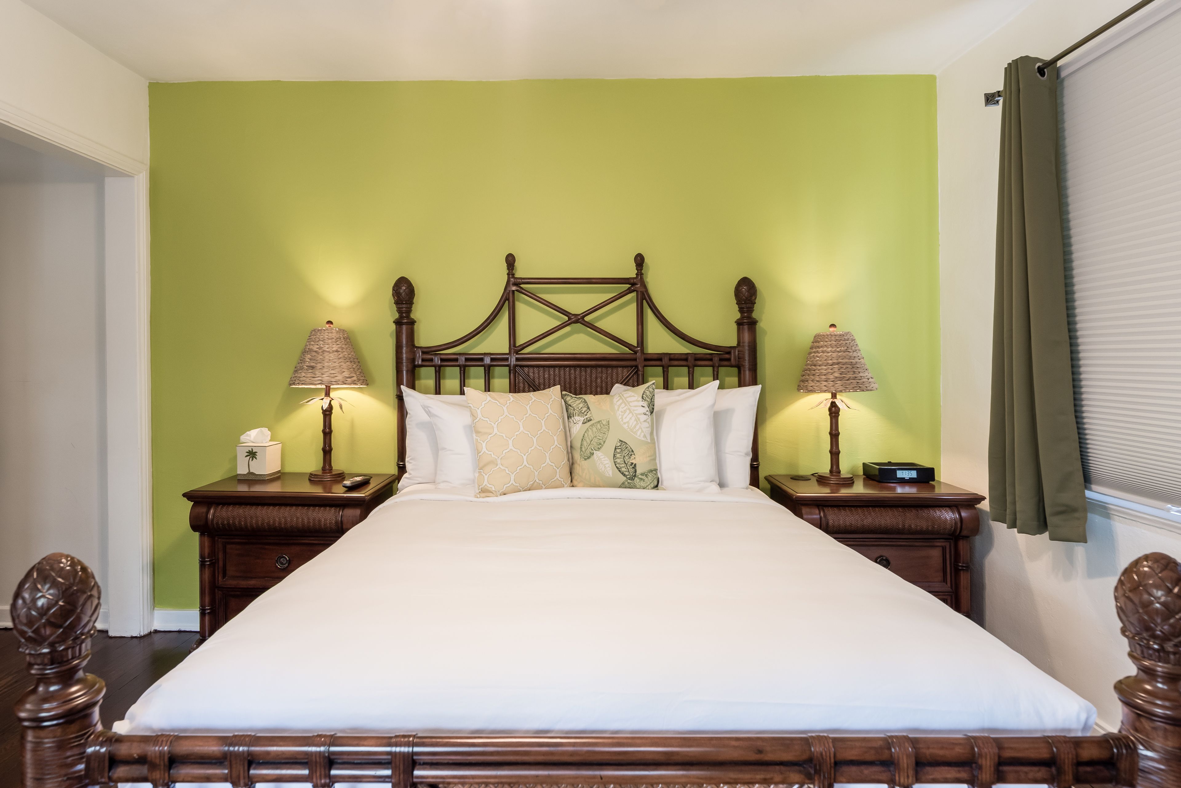 A neatly made bed with a wooden headboard, two bedside tables with lamps, and a green wall.