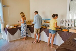 Una mesa de desayuno buffet cubierta con mantel marrón y blanco, con comida y un dispensador de bebidas.