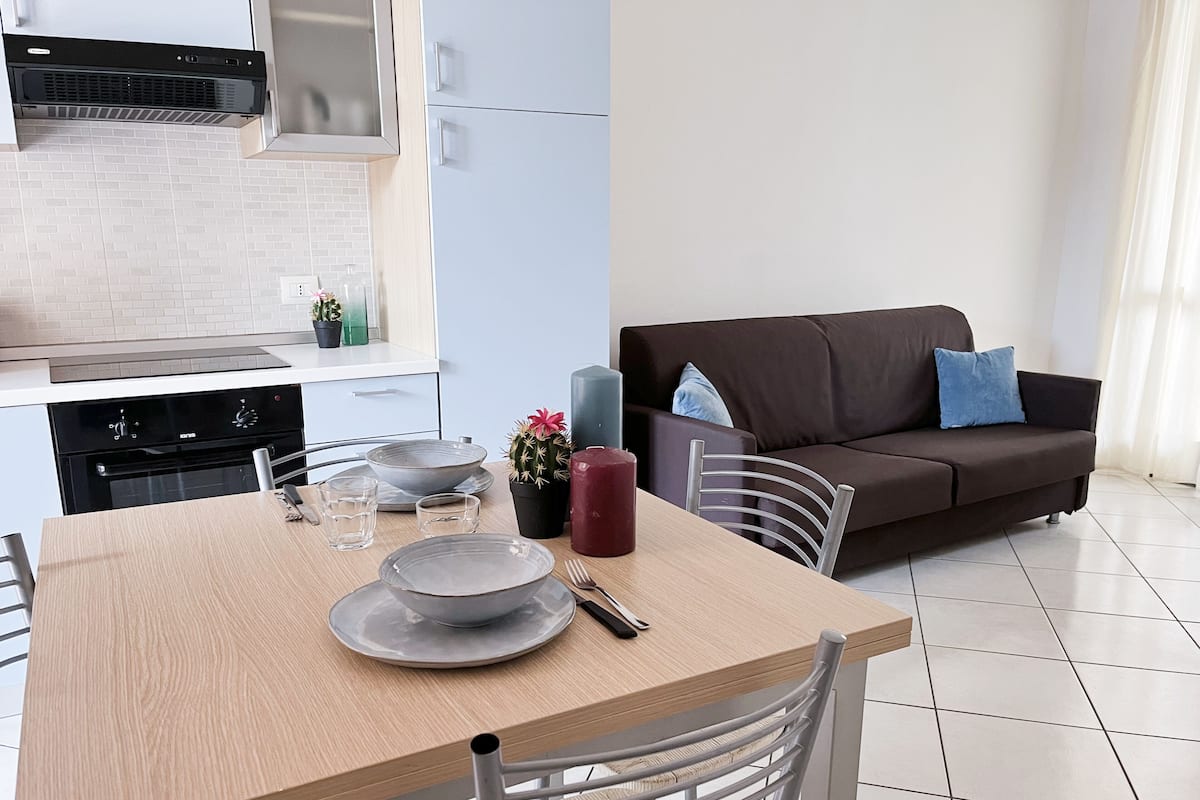 A modern kitchen with a dining table set for two, a sofa, and a cactus plant.