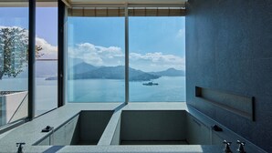 A modern bathroom with a large bathtub and a glass-enclosed shower area, offering a scenic view of a lake and mountains. - GRAND HILAI SUN MOON LAKE (Yuchi)