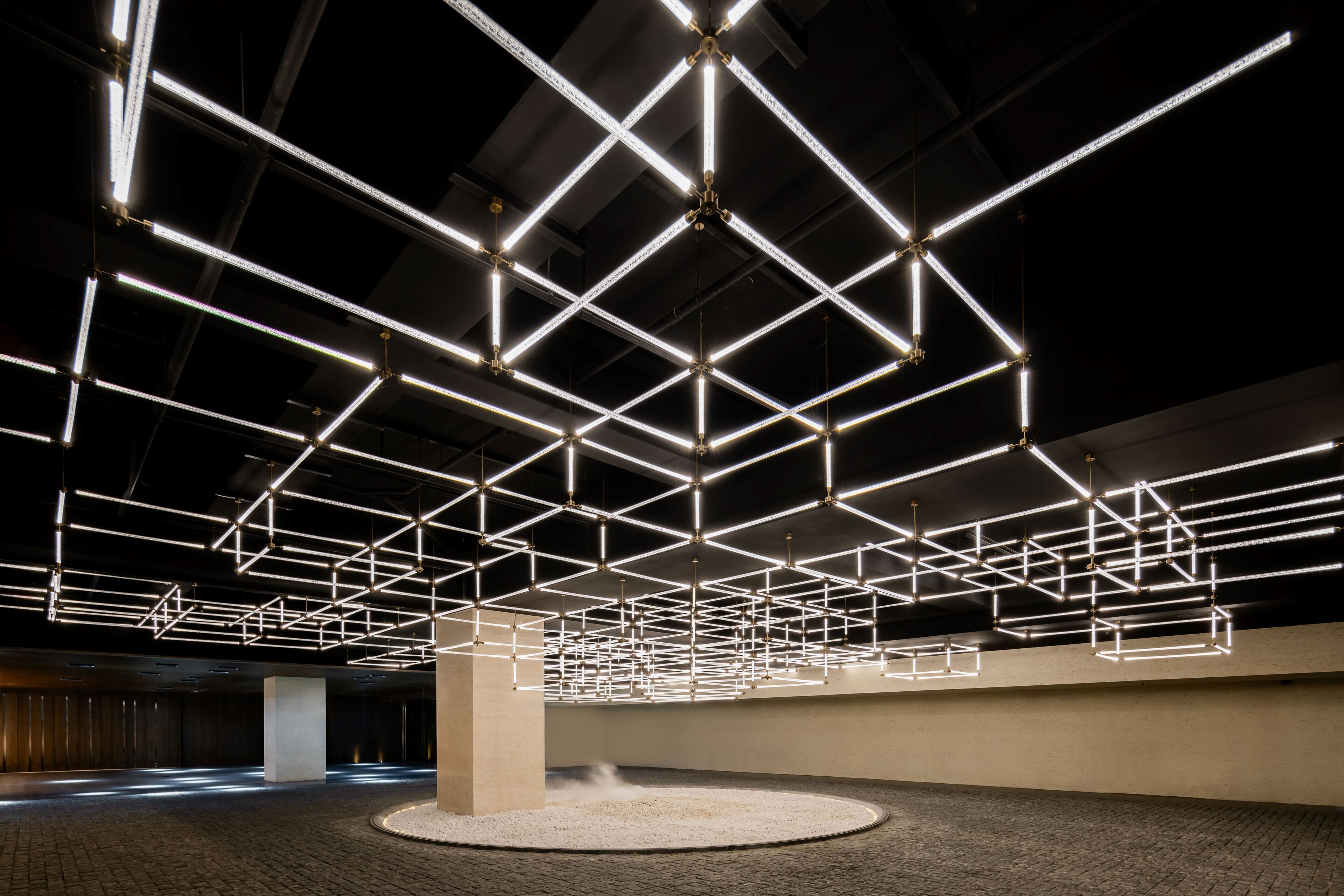A spacious indoor area with a high ceiling and a grid of illuminated linear lights.