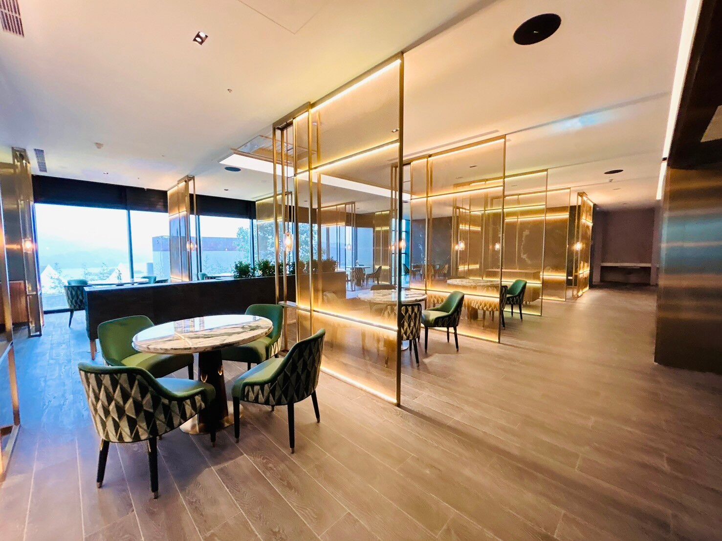 Un interior moderno con un separador de vidrio, piso de madera y sillas tapizadas en verde.