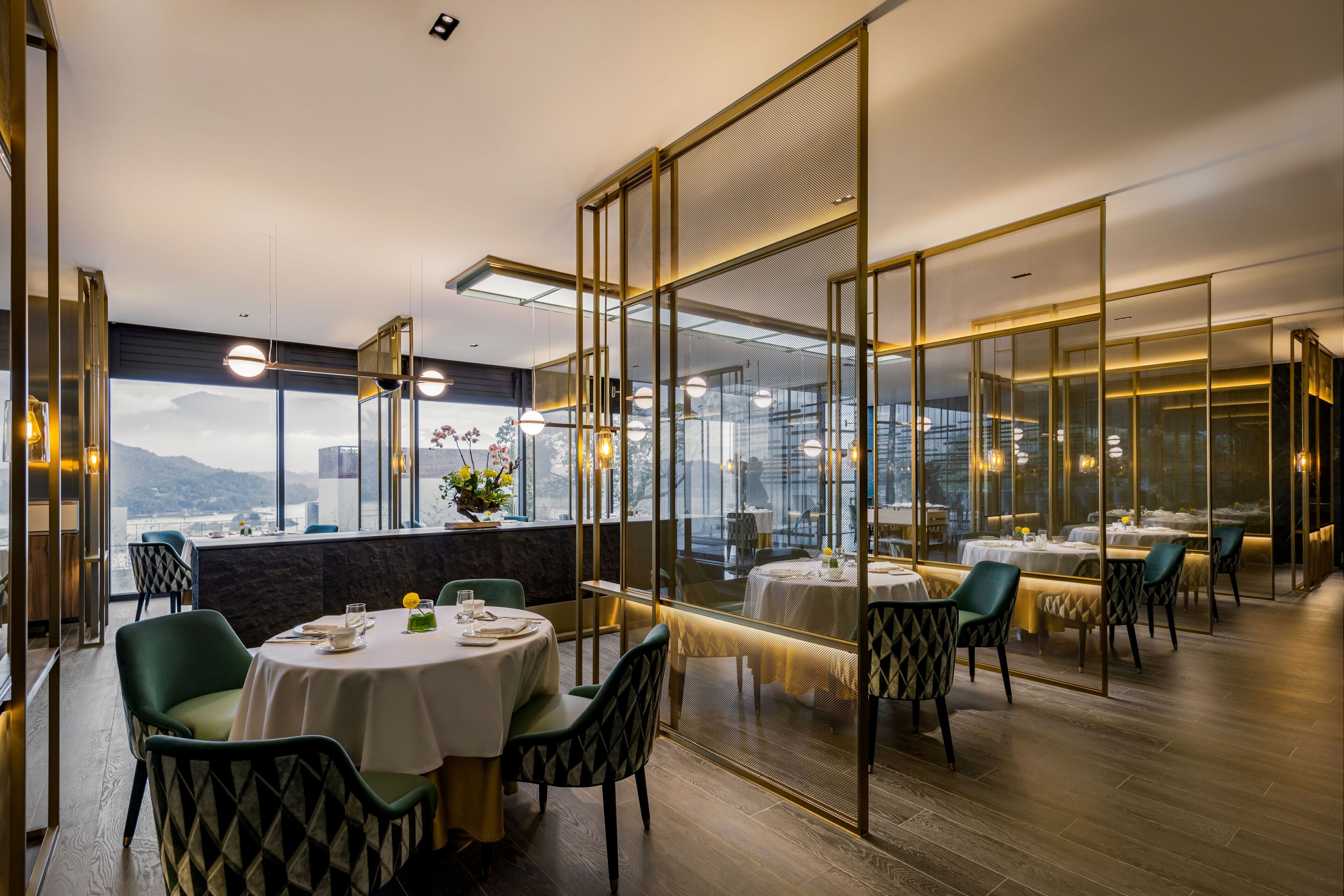 A restaurant with round tables, green chairs, and a view of a cityscape through large windows.