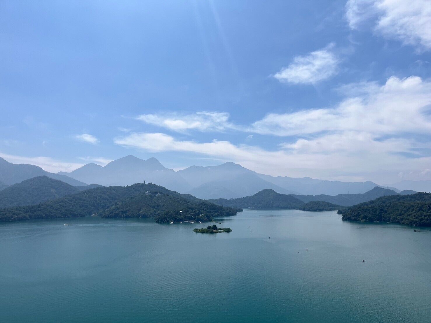 A panoramic view of a lake surrounded by mountains, with a small island in the center.