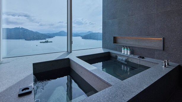 A modern bathroom with a large bathtub, a glass-enclosed shower, and a view of a lake with mountains in the background. - GRAND HILAI SUN MOON LAKE (Yuchi)
