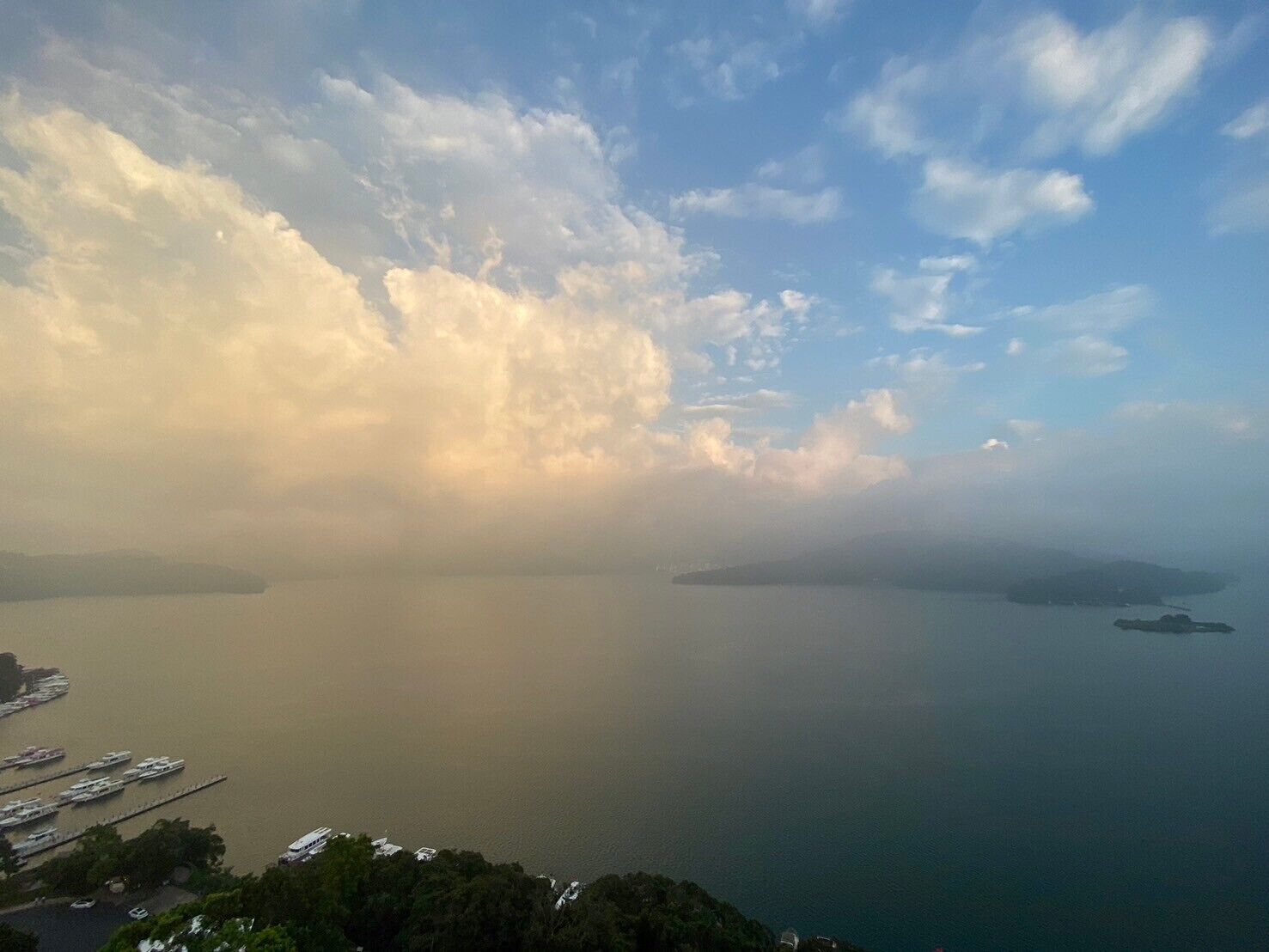 A coastal view with a marina, calm sea, and distant islands under a partly cloudy sky.