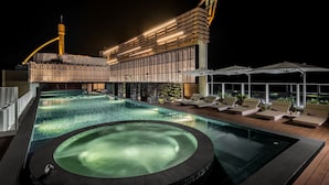 A rooftop swimming pool with lounge chairs and a hot tub, surrounded by a modern building with large windows and a crane. - GRAND HILAI SUN MOON LAKE (Yuchi)