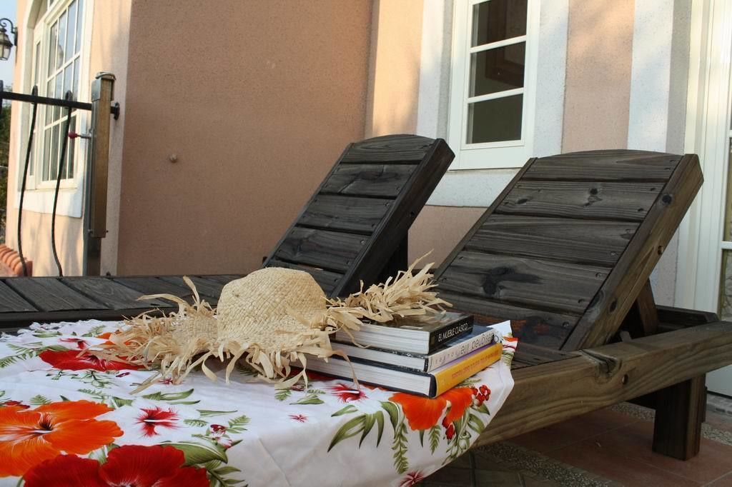 A sun lounger with a woven hat and books, set on a floral tablecloth.