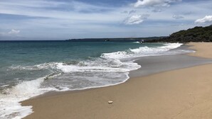 Una spiaggia con acque cristalline, una riva sabbiosa e una costa rocciosa in lontananza, il tutto sotto un cielo parzialmente nuvoloso.