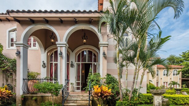 Un edificio in stile mediterraneo con portali ad arco, tetto in tegole e un giardino curato con palme e piante.