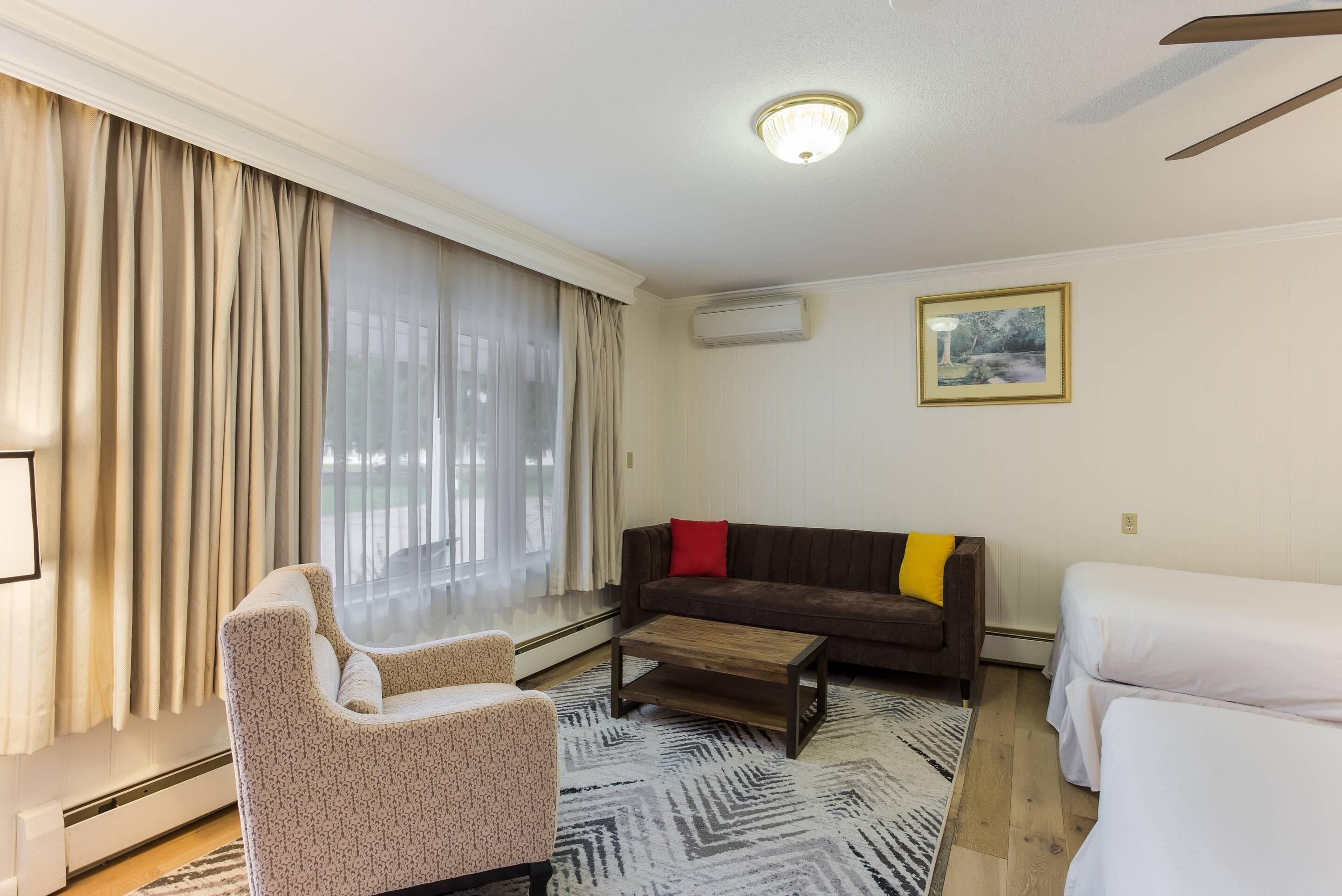 Una habitación de hotel moderna con sofá, sillón y una pequeña mesa.