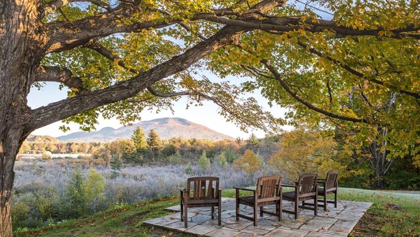 A patio with four wooden chairs and a table set on a stone platform, overlooking a natural landscape with trees and distant hills. - The Palmer House Resort, an Ascend Collection Hotel (Manchester Center)