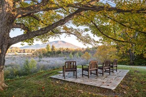 A patio with four wooden chairs and a table set on a stone platform, overlooking a natural landscape with trees and distant hills. - The Palmer House Resort, an Ascend Collection Hotel (Manchester Center)