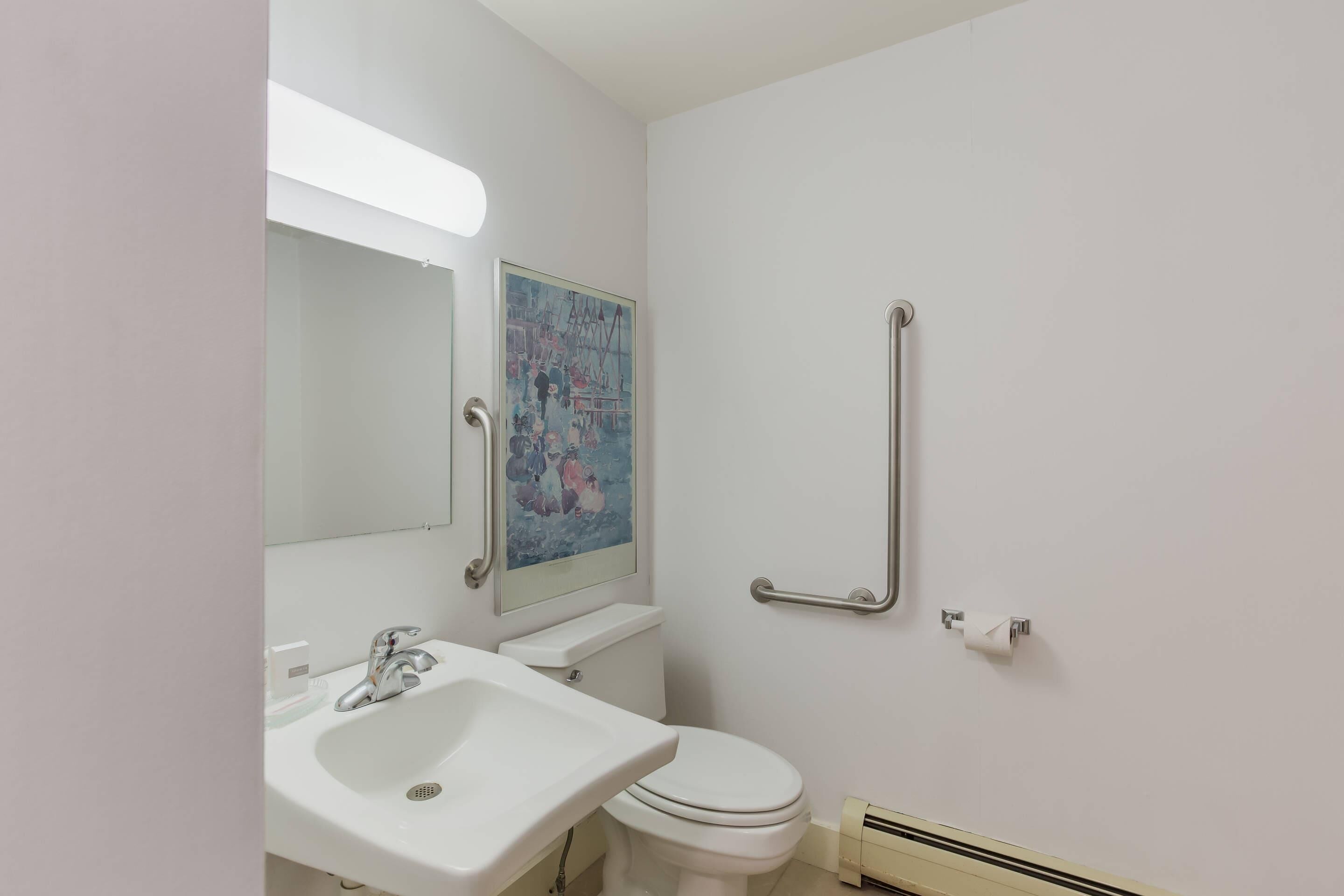 A bathroom with a white sink, toilet, and handrails.