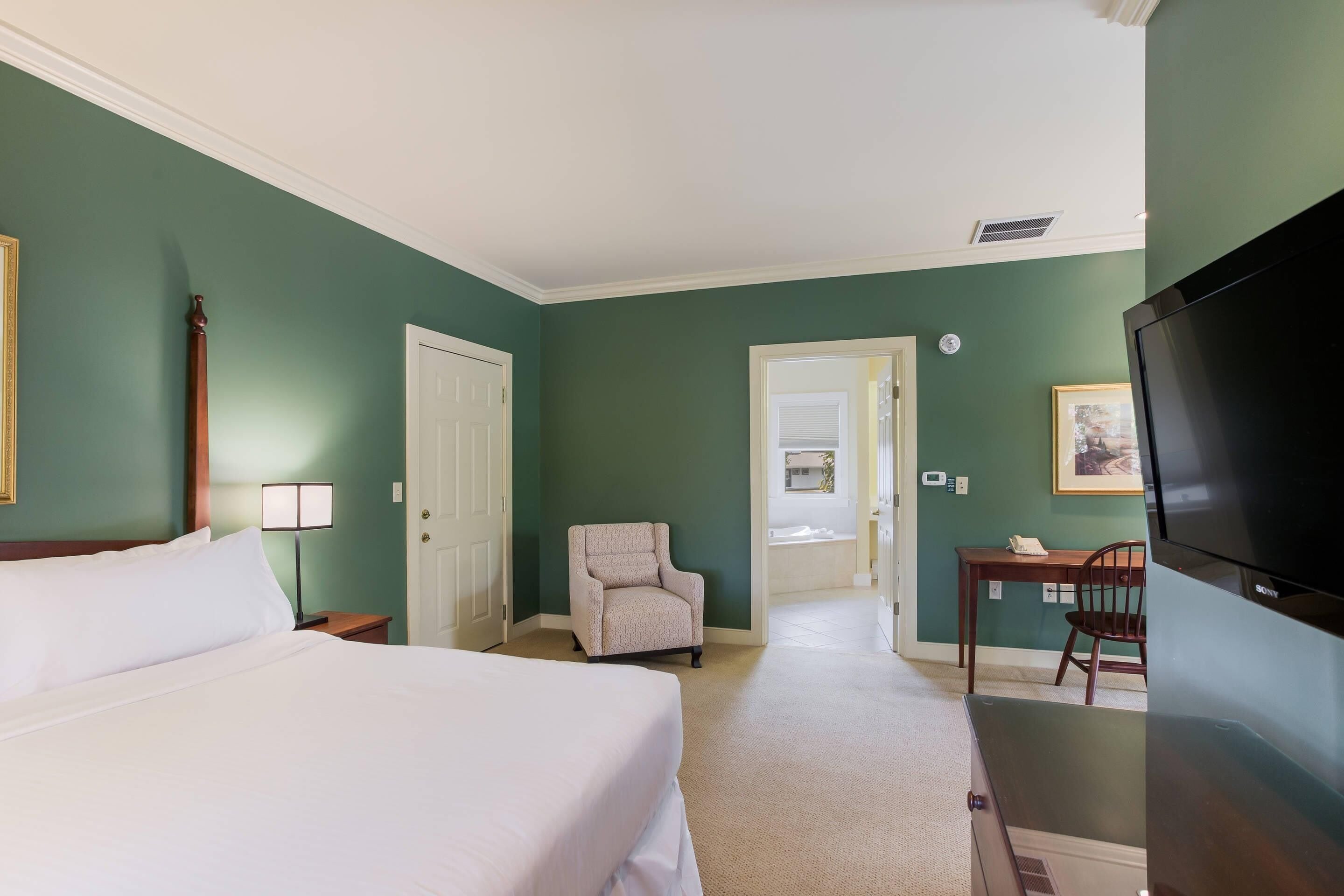 A hotel room with a bed, a chair, a desk, and a television.