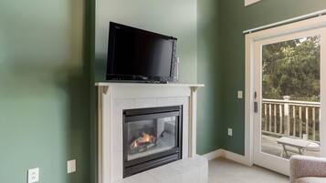 A living room with a fireplace, a television on top, and a view of the outdoors through a sliding glass door.